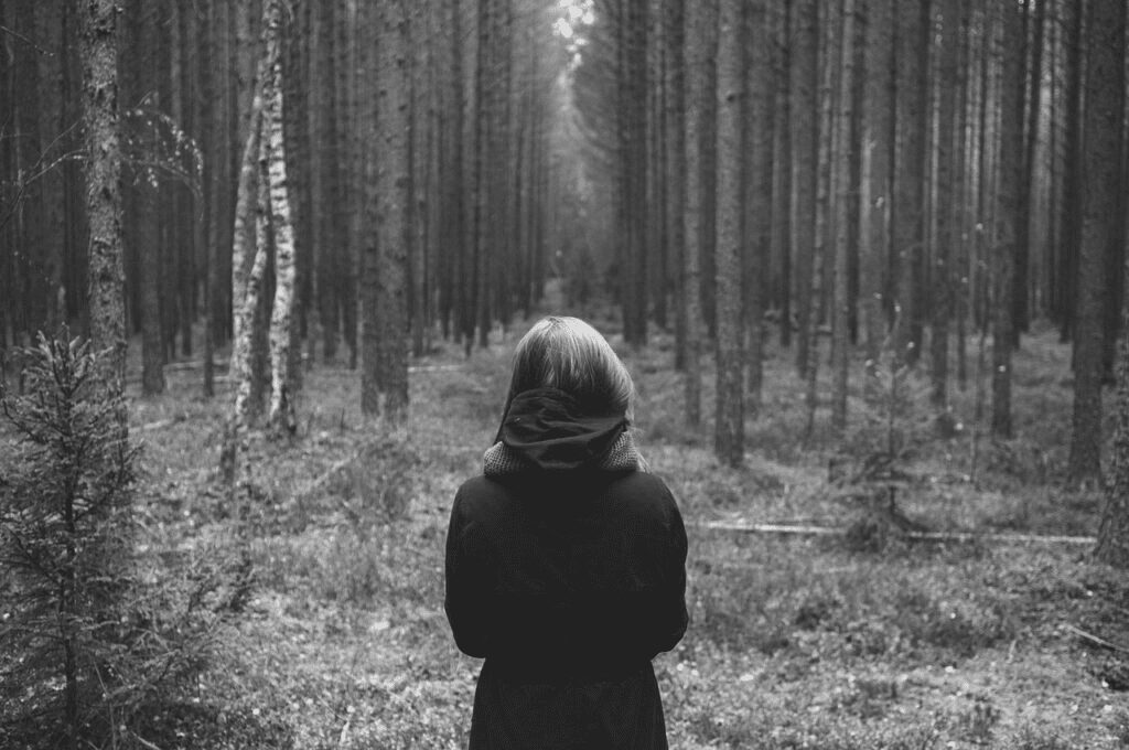 A woman standing in the woods looking at trees.
