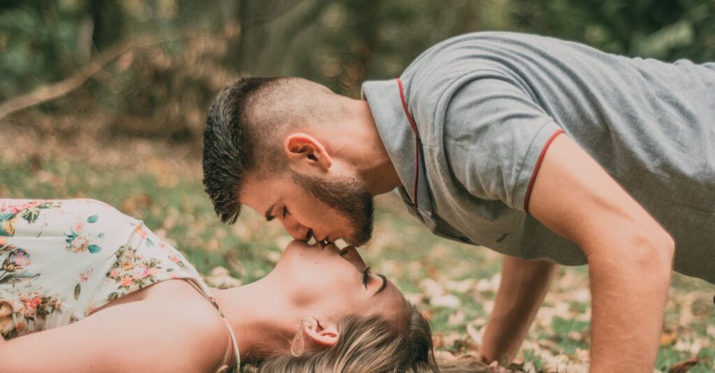 Young couple kissing on grass surrounded by fallen autumn leaves.