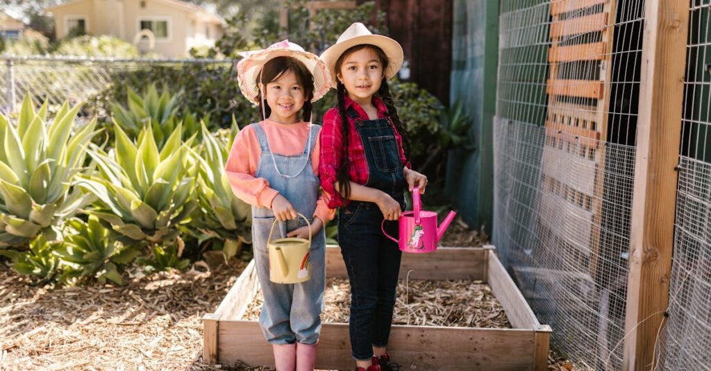 Two young girls wearing hats and overalls, happily watering plants in a garden.