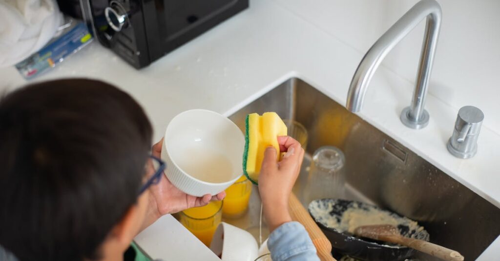 A young boy diligently washing dishes with a sponge in the kitchen sink.