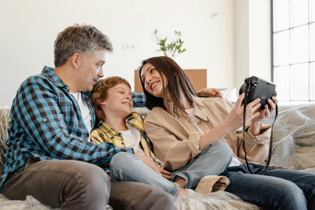 Happy family sitting on sofa, enjoying a Polaroid camera at home.