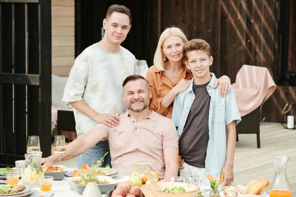 Family of four dining outdoors in a cheerful atmosphere with a table full of food and beverages.