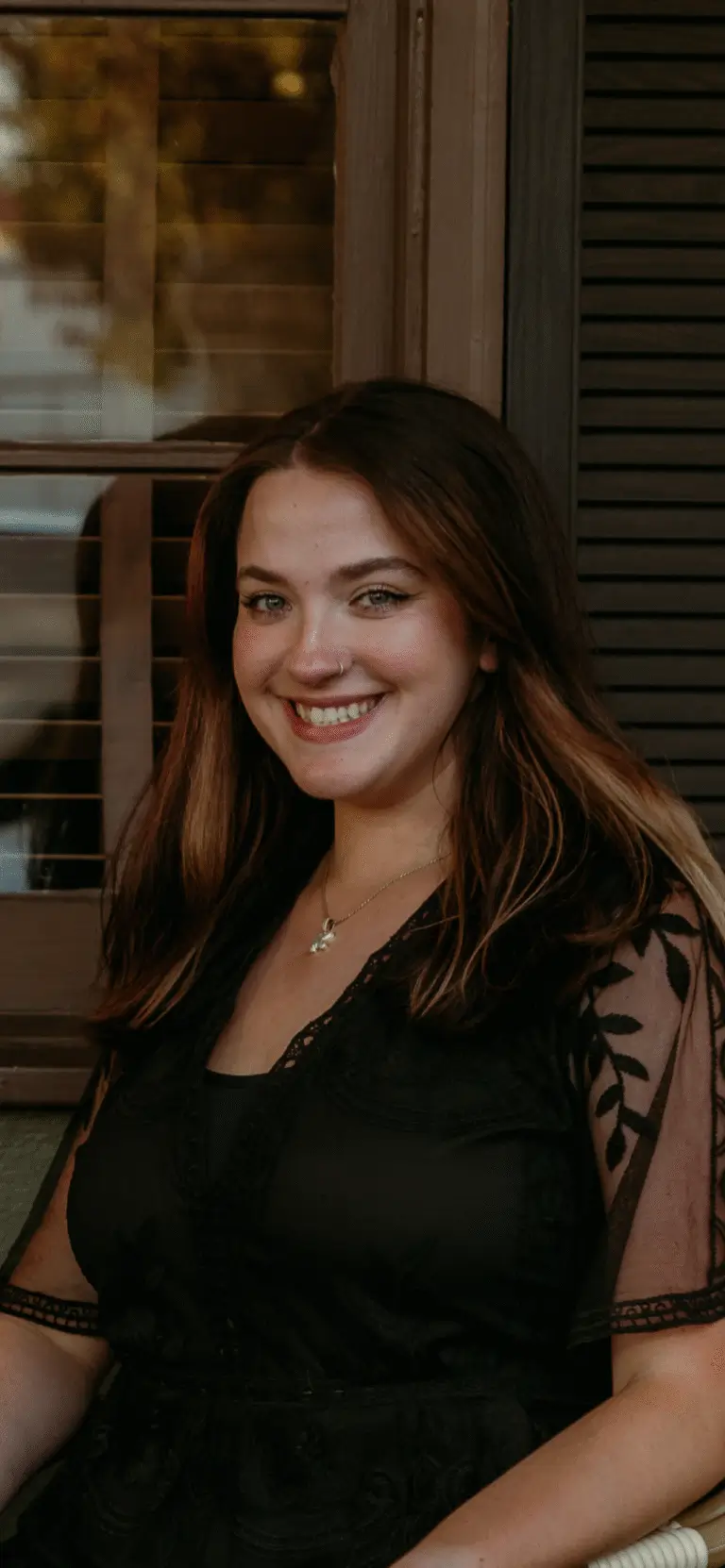 Smiling woman in black dress, seated indoors.