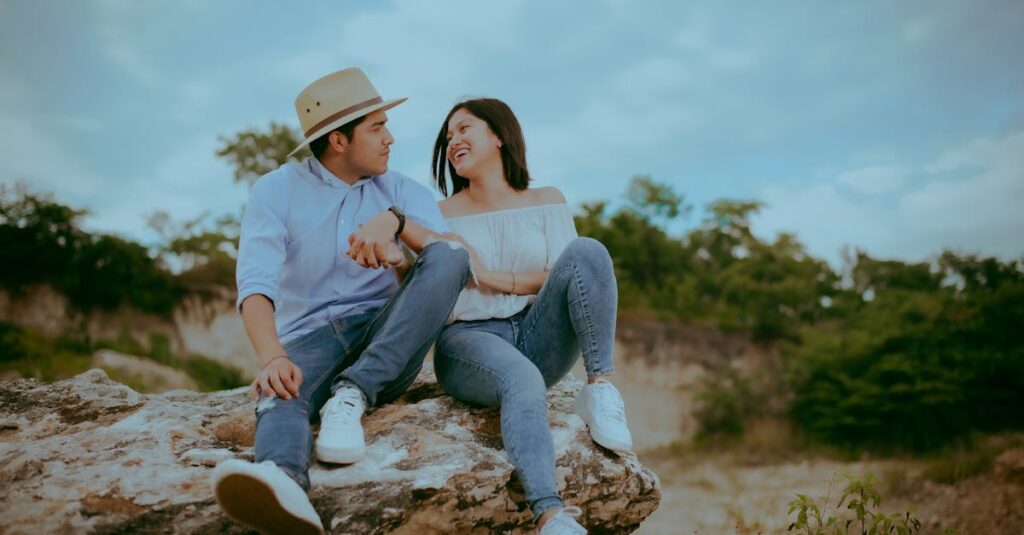 A happy couple sitting on a rock, sharing a joyful moment outdoors in nature.